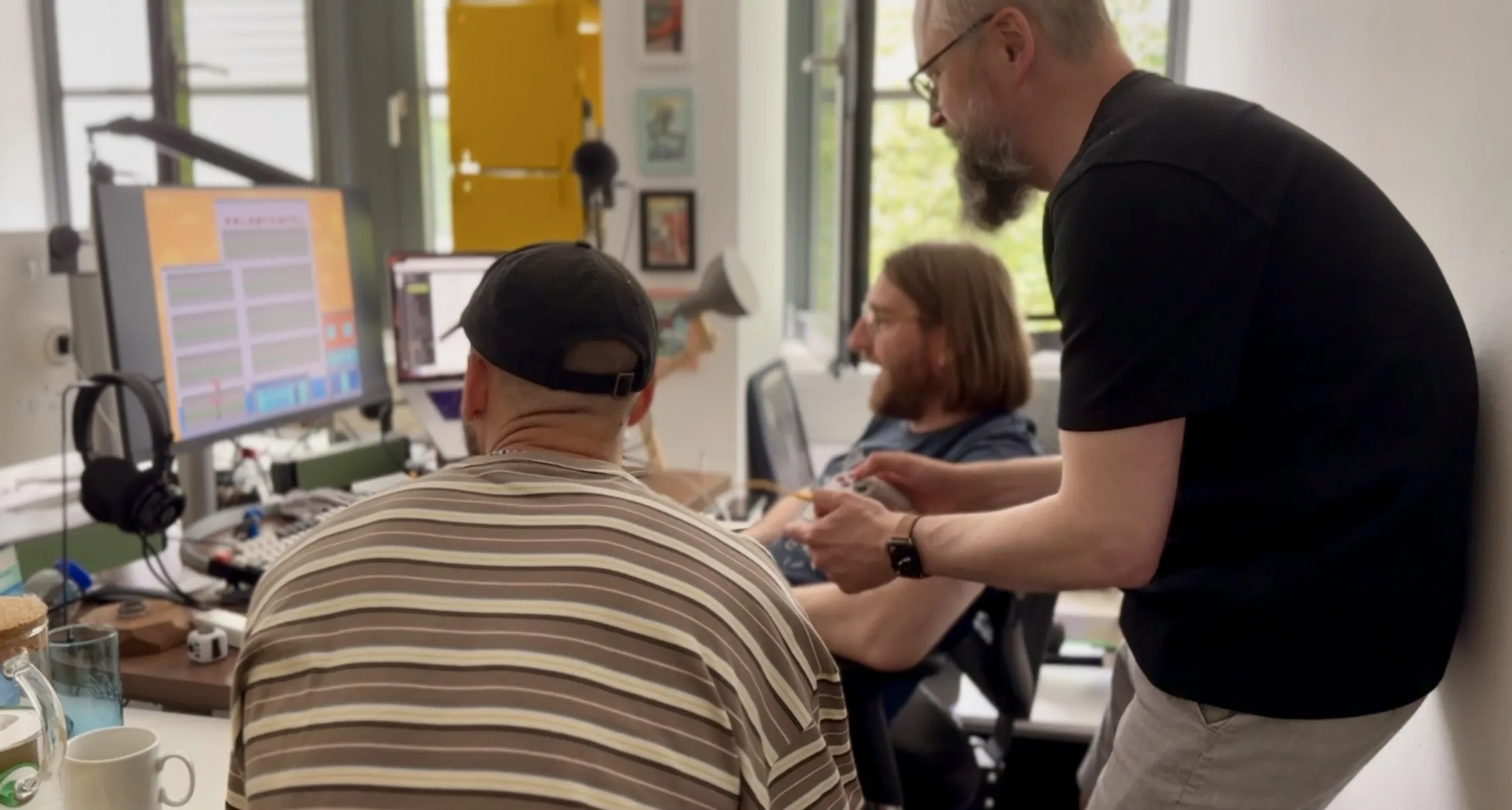 Three people in an office testing a pixel-style game on a monitor